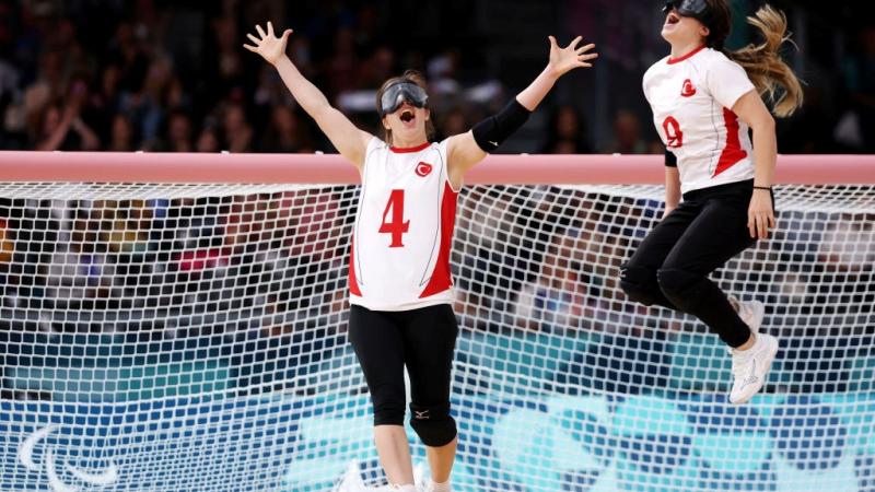 Two female goalball athletes celebrate in front of a net